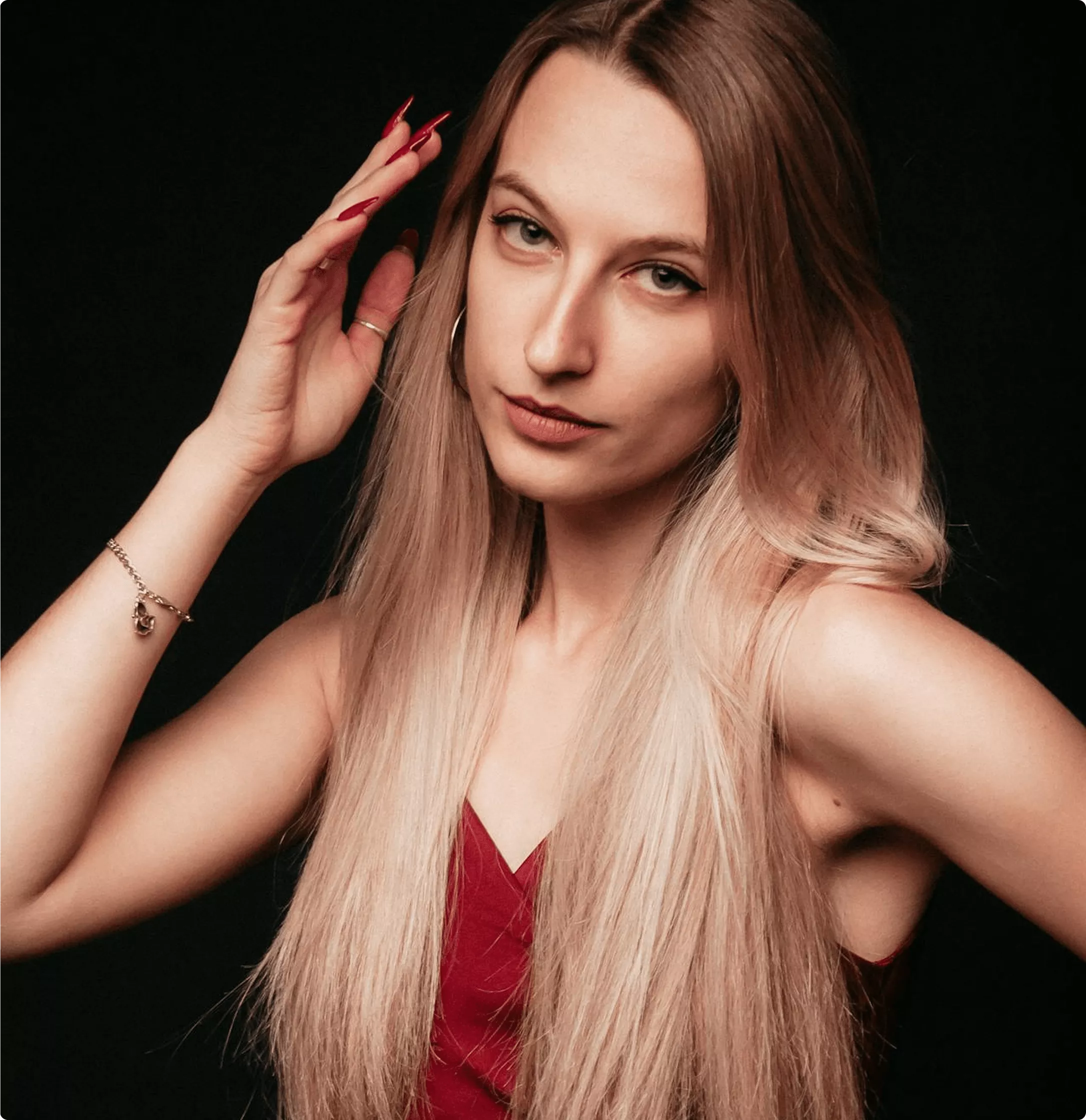 Woman with pale blonde long straight hair wearing dark red V-neck top against black background