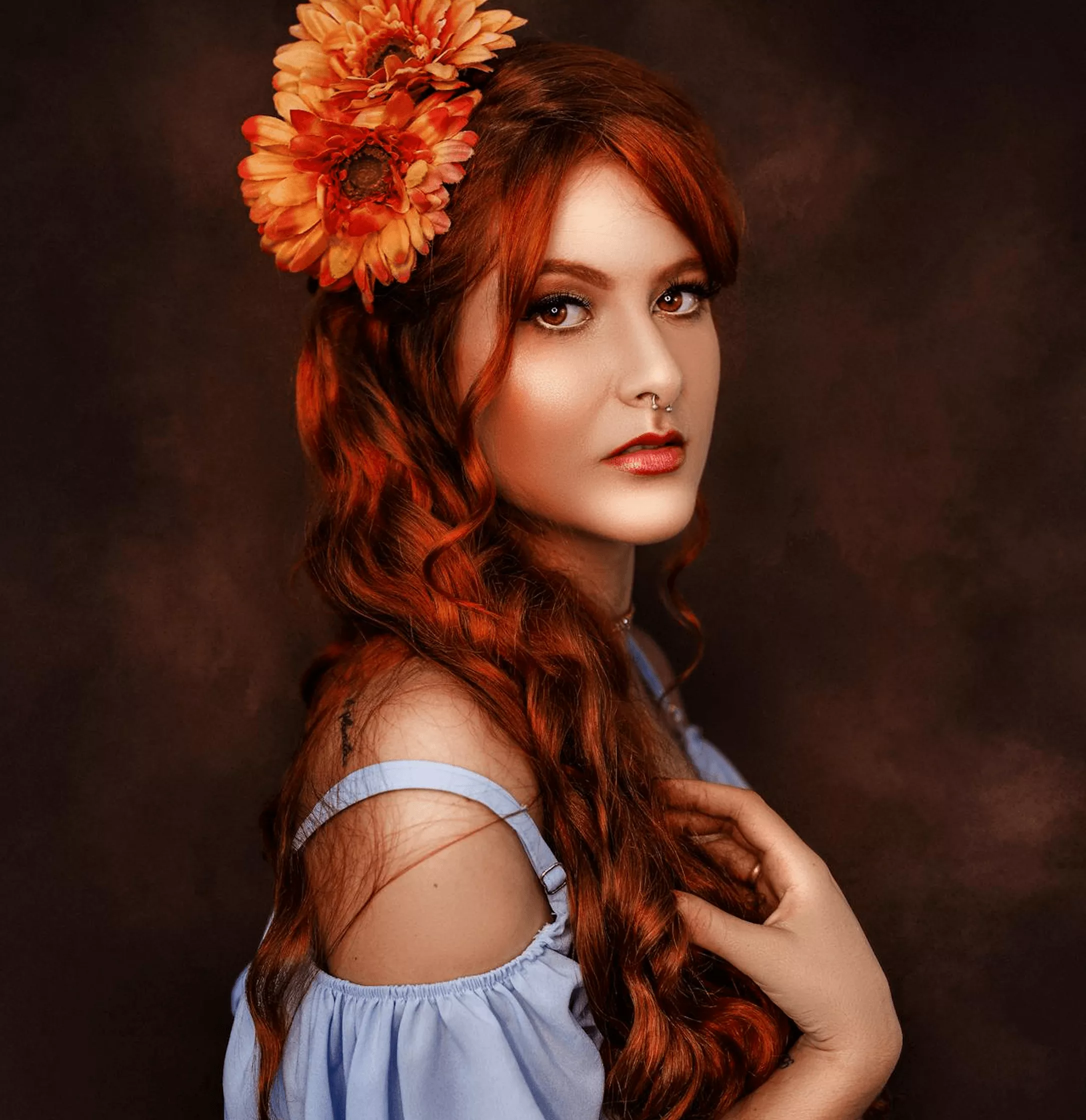 Woman with long red-orange wavy hair styled with red flower accessory wearing light blue off-shoulder dress