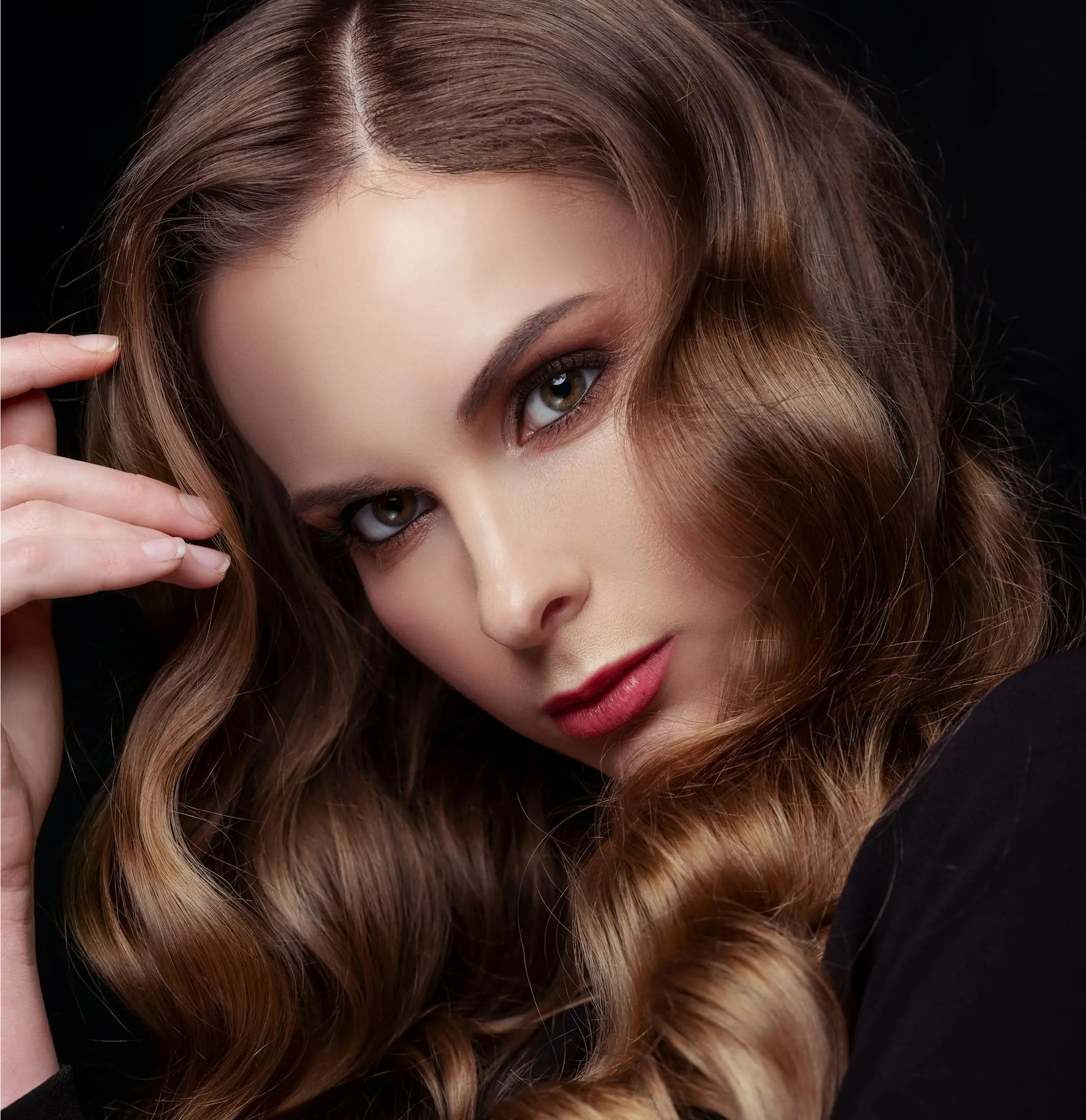 Woman with chestnut brown wavy hair in side profile wearing dark clothing against dark background