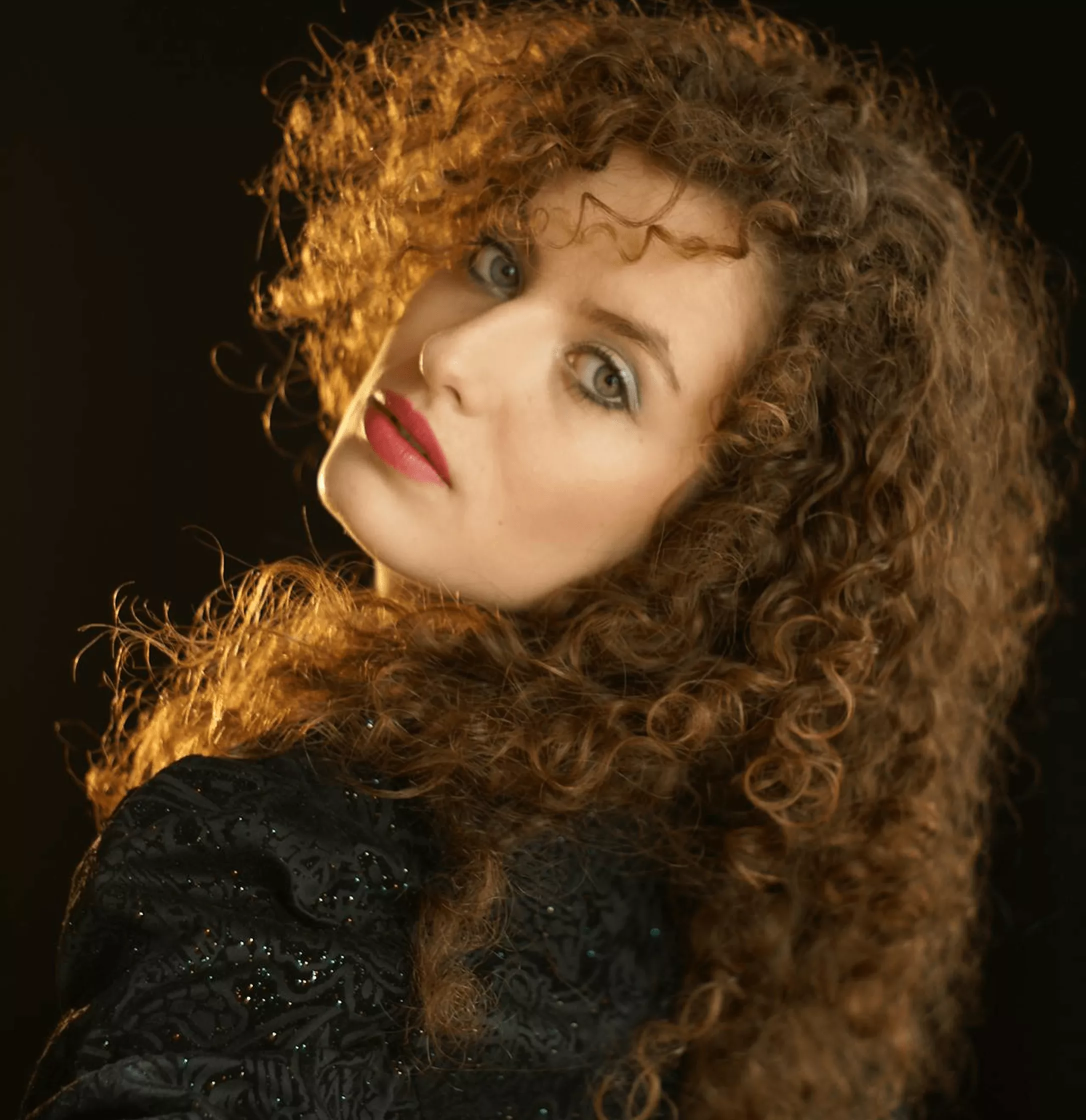 Woman with honey-brown curly textured hair in gold lighting wearing sparkly black sequin outfit