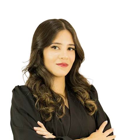 A woman with long dark wavy hair, wearing a black blazer with arms crossed, conveying a composed, professional demeanor against a black background.
