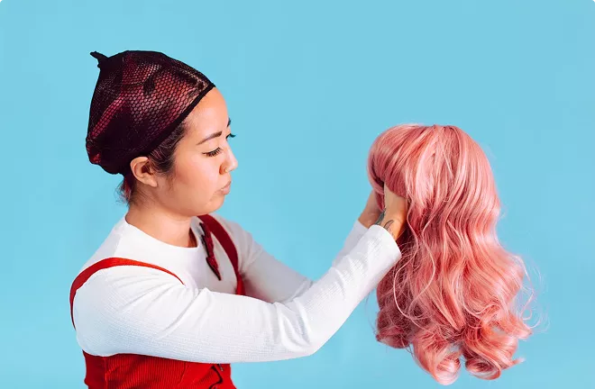 Two people sharing a joyful moment—one with bright pink wavy hair in a patterned orange top, the other with dark curly hair in a pink shirt—celebrating together.