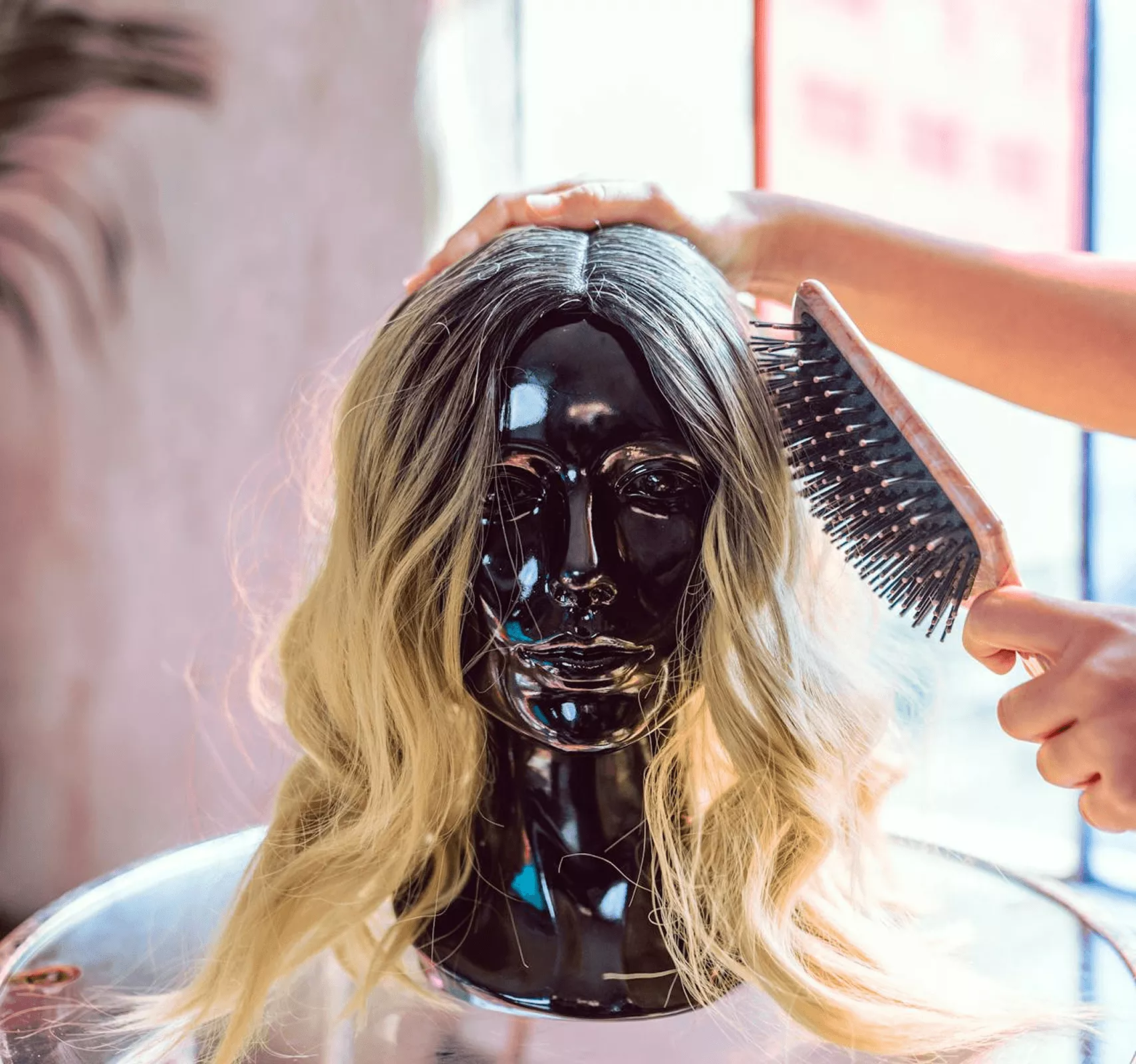 Blonde wig on black mannequin head being styled and brushed with wooden comb styling tools