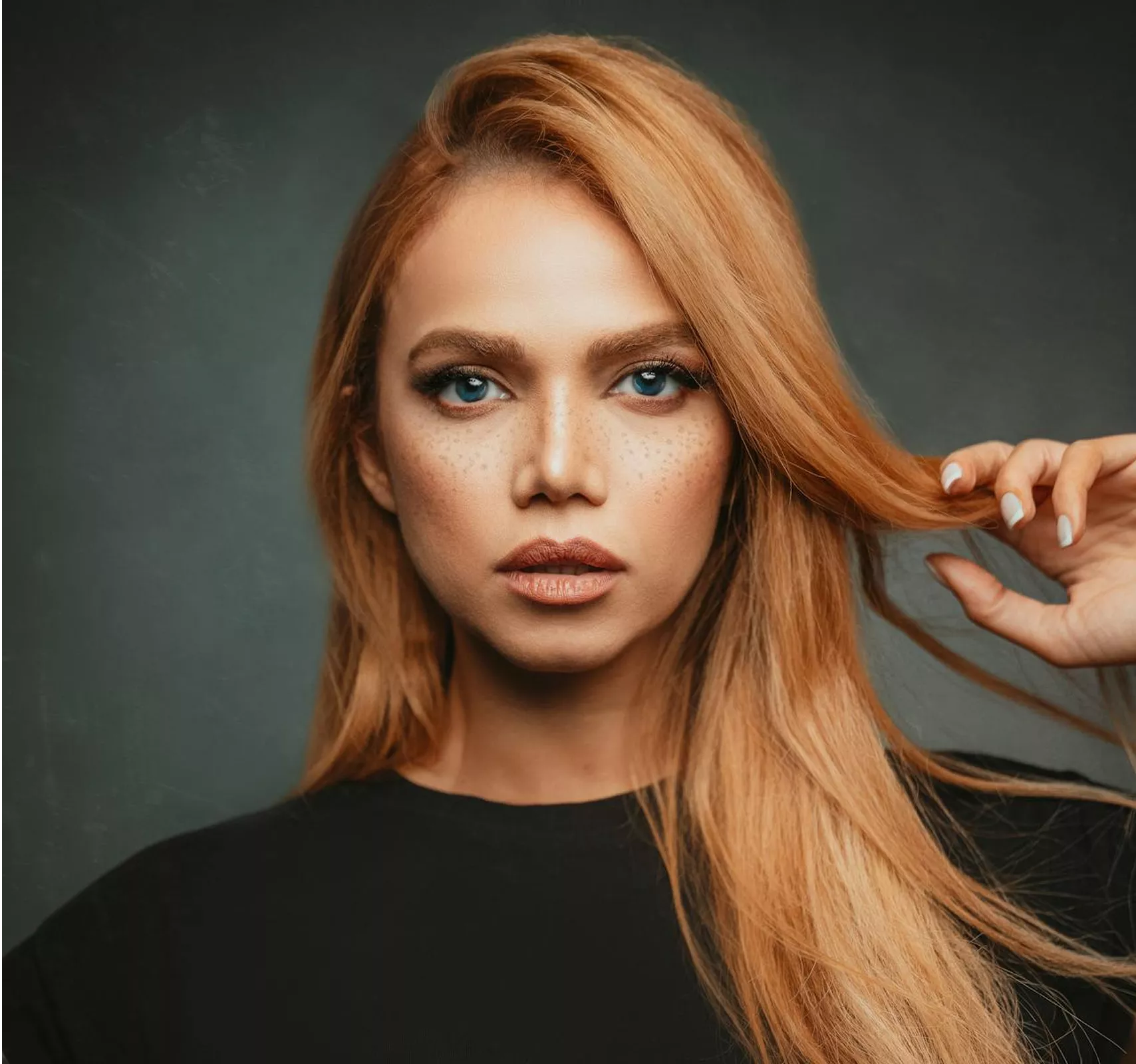 A polished portrait of someone with smooth copper-auburn hair and professional makeup against a muted teal background—conveying expertise and trustworthiness.