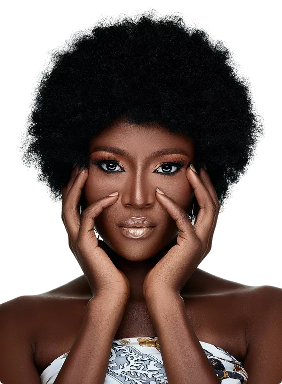 A woman with a large natural afro and glam makeup resting her face in both hands against a bright pink background.